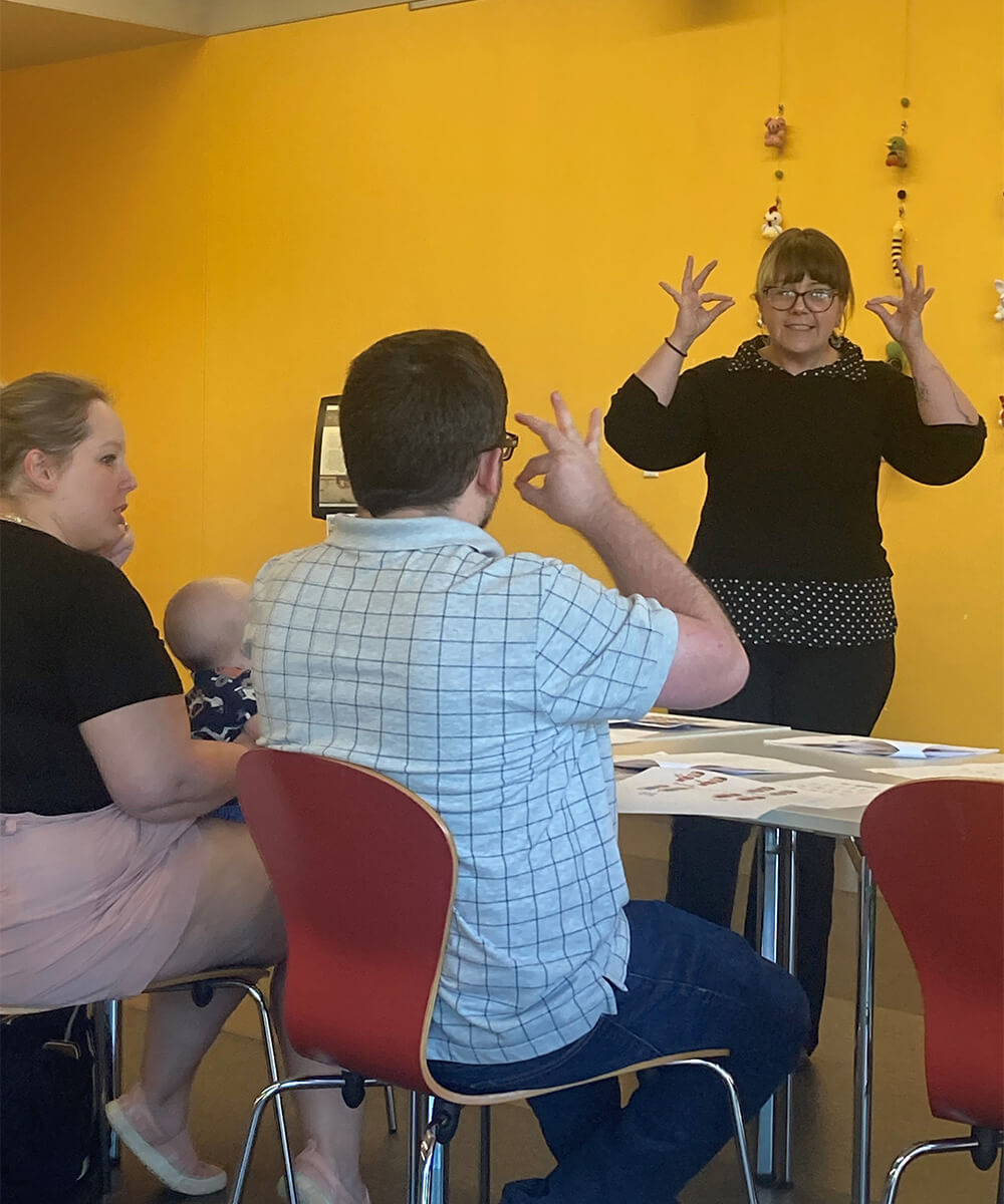 A woman doing ASL signs to a man, woman, and baby. 