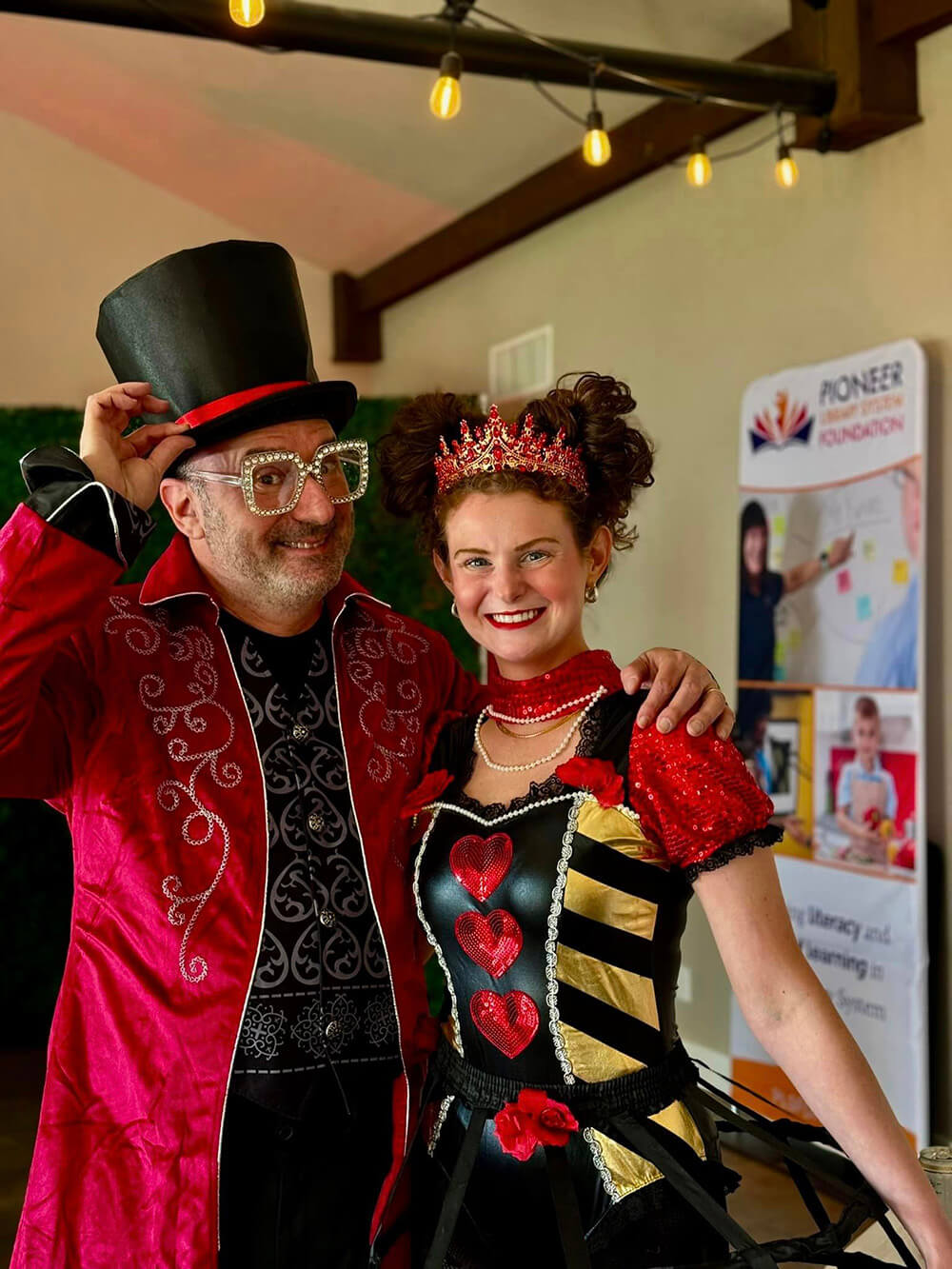 A man dressed as the Mad Hatter smiles with a woman dressed as the Queen of Hearts.