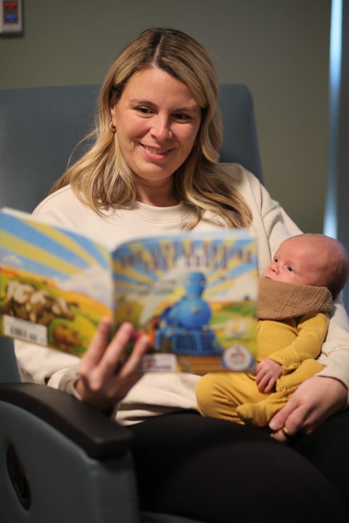 A mom holds her newborn baby while reading him a book.