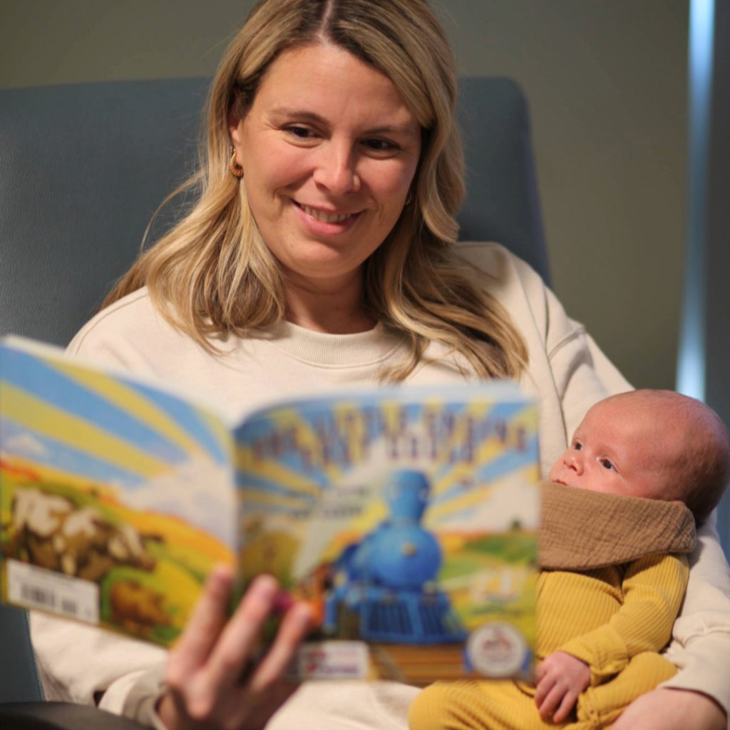 A mom holding her baby and reading to him from a book.
