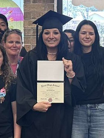 Casey Cook Excel HS graduate A woman in a cap and gown is holding a diploma with her family beside her.