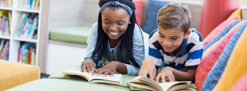 SLC a young girl and young boy are reading books together in a library.