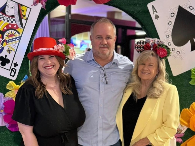 A man, center, stands with two women wearing hats.